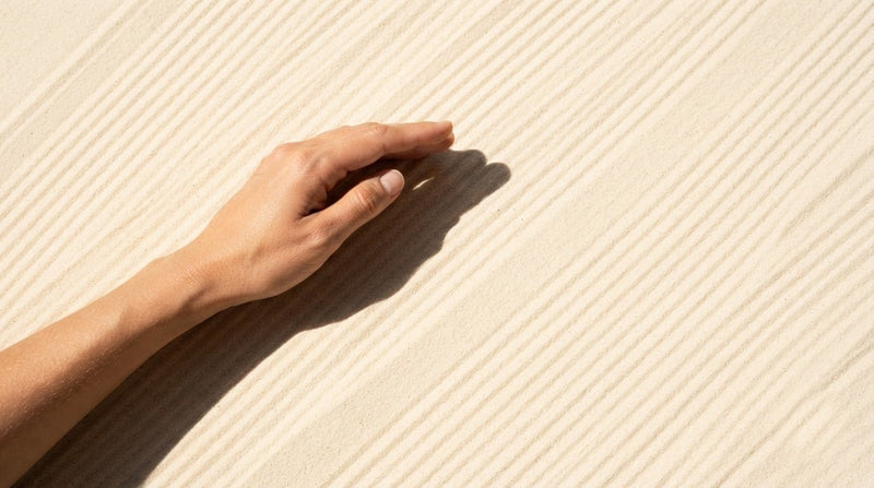 The hard shadow of a hand across sunlit sand