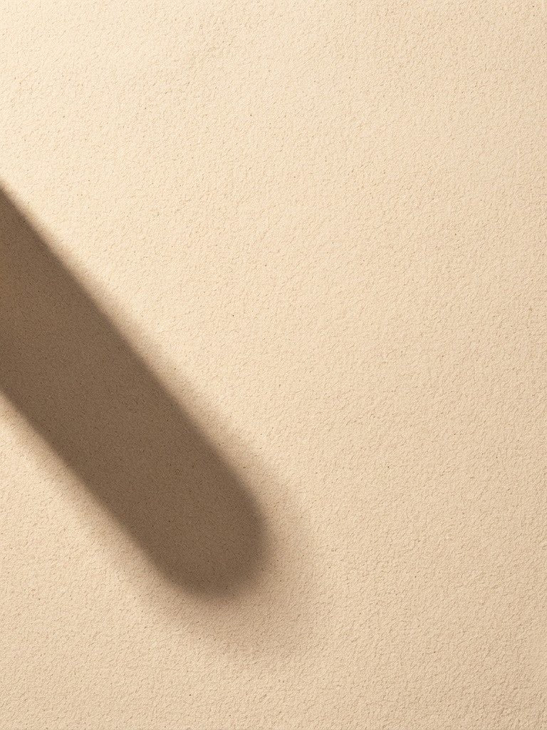 A long hard shadow falling across dry sand in strong sun